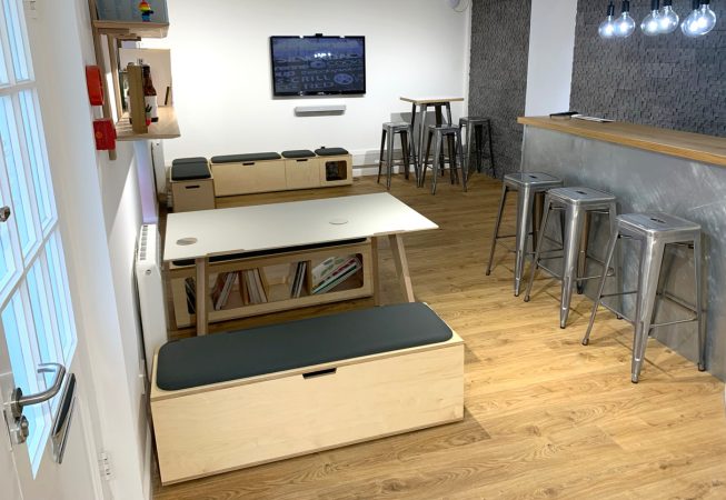 Office reception breakout space, with wooden plywood storage benches, with upholstered seat pads in grey fabric